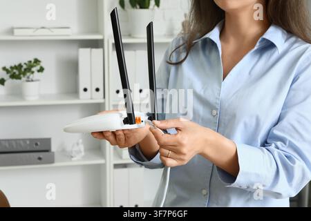 Femme connectant un câble Ethernet à un routeur sans fil blanc avec antennes dans un cadre de bureau moderne, l'appareil dispose d'antennes pour un signal amélioré Banque D'Images