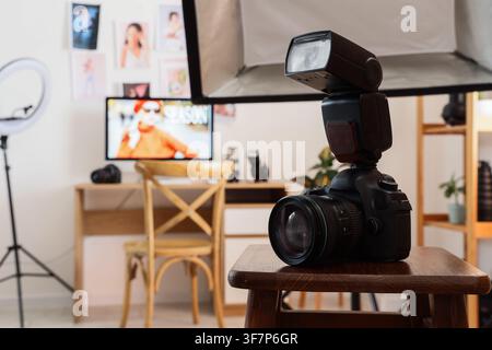 Appareil photo reflex numérique avec un flash externe posé sur un tabouret en bois dans un studio de photographie domestique, l'arrière-plan montre un bureau avec un compu Banque D'Images