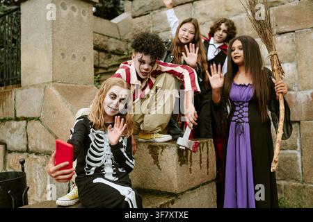 Divers adolescents en costumes d'Halloween prenant un selfie sur un smartphone Banque D'Images
