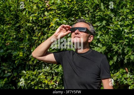 Un homme en t-shirt noir observe l'éclipse solaire avec des lunettes de protection oculaire Banque D'Images