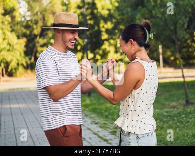 Un couple joyeux se tient la main et sourit dans le parc par une journée d'été ensoleillée. Banque D'Images
