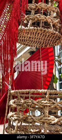 Un éventail pliant rouge est encadré par des paniers tissés suspendus et la longue frange d'un textile rouge dans une installation décorative détaillée de Cruces de Mayo. G Banque D'Images