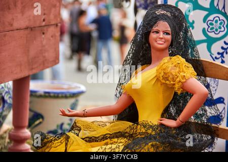 Une poupée décorative vêtue d'une robe flamenco jaune vif avec de la dentelle noire et une mantille en dentelle noire est exposée parmi des céramiques traditionnelles Banque D'Images