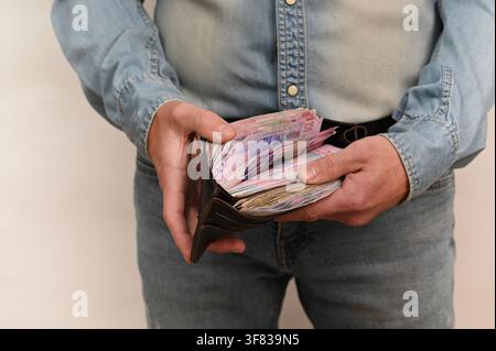 Portemonnaie ouvert avec des billets colorés en hryvnias ukrainiens visibles, des mains le tenant. L'argent dans le portefeuille représente les économies personnelles, la gestion financière Banque D'Images