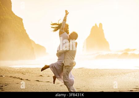 Couple profitant d'un moment joyeux sur la plage de Reynisfjara au coucher du soleil avec des falaises marines en arrière-plan Banque D'Images