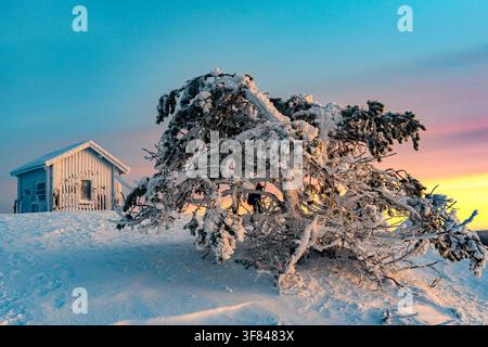 Une cabane de montagne gelée se dresse à l'aube en Laponie avec un ciel coloré et un paysage enneigé Banque D'Images
