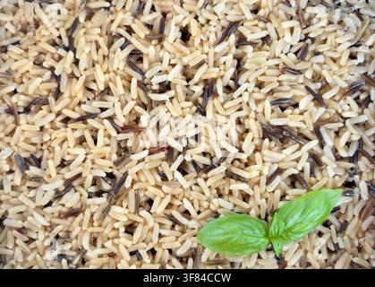 Fond avec un mélange de riz brun et de riz sauvage cuits et de feuilles de basilic frais. Concept de régime méditerranéen, nutrition équilibrée et style de vie bien-être. Banque D'Images