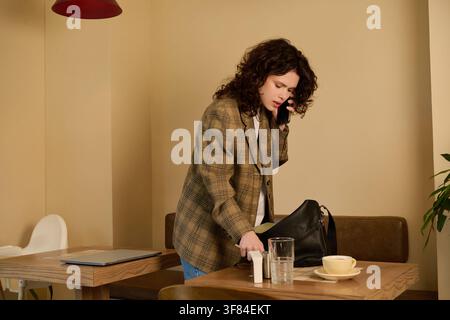 Femme aux cheveux bouclés travaille à distance à une table confortable d'un café tout en étant au téléphone Banque D'Images