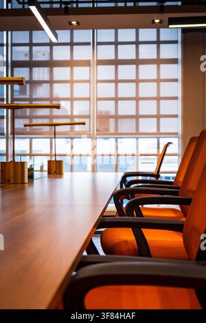 Salle de conférence moderne avec table en bois, chaises orange et lampes de table en laiton, intérieur de salle de réunion vide. Banque D'Images