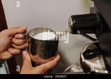 Barista chauffant du lait à l'aide d'une machine à expresso professionnelle pour obtenir une micro-mousse crémeuse. Technique essentielle pour préparer des boissons au café spécialisées. Banque D'Images