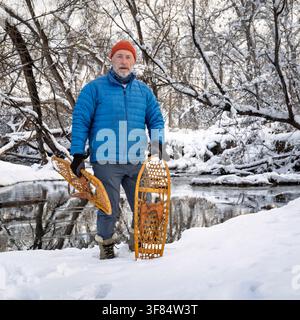Homme âgé avec des raquettes en bois classiques (Bear Paw) sur une rive de ruisseau, paysage d'hiver au Colorado Banque D'Images