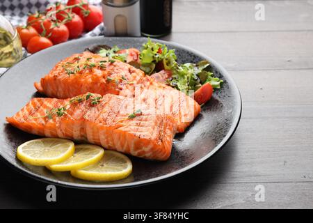 Morceaux de saumon grillé servis avec de la salade sur une table en bois, gros plan. Espace pour texte Banque D'Images