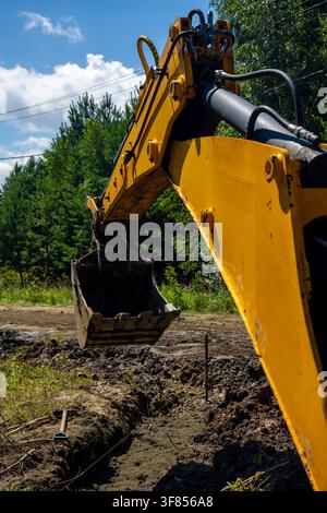 Bras de pelleteuse jaune creusant une tranchée sur une route de campagne en plein air par temps ensoleillé. Concept : travaux de creusement pour les services publics Banque D'Images