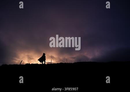 Silhouette d'un randonneur solitaire portant un poncho au coucher du soleil dans le páramo de haute altitude du parc national de Cajas, Équateur Banque D'Images