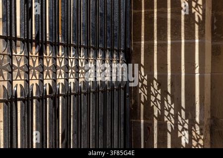 Les rampes en fer forgé avec des motifs de croix maltaise projetaient des ombres dramatiques et motifs sur un mur en calcaire à Malte Banque D'Images
