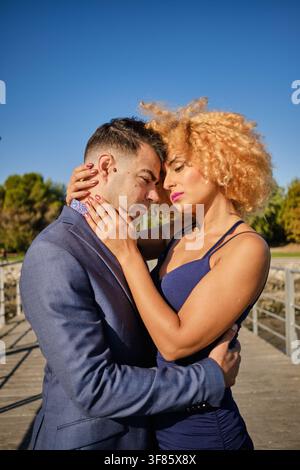 Couple enlacé sur un pont, partageant un moment intime sous un ciel bleu clair Banque D'Images