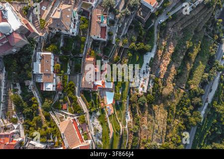 Vue aérienne du village en colline aux toits en terre cuite, aux jardins en terrasses et aux routes sinueuses surplombant le paysage méditerranéen à Raito, Am Banque D'Images