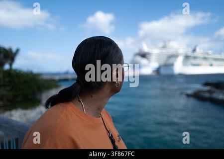 Femme portant un haut orange et des lunettes de soleil contemplant une marina de yachts blancs et une eau bleue claire. Banque D'Images