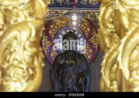 Un Bouddha debout devant un mandala rouge richement décoré rayonne d'une dignité calme et d'une sérénité intemporelle, des piliers dorés encadrent la scène comme une porte Banque D'Images