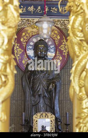 Un Bouddha debout devant un mandala rouge richement décoré rayonne d'une dignité calme et d'une sérénité intemporelle, des piliers dorés encadrent la scène comme une porte Banque D'Images