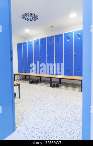 Vestiaire avec casiers bleus et vue sur des chaussures, bancs en bois et murs blancs Banque D'Images