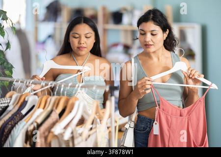 Deux jeunes femmes choisissant des robes et des hauts en magasin Banque D'Images