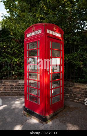 Cabine téléphonique britannique rouge traditionnelle debout à côté d'un mur de briques et d'arbres feuillus. Banque D'Images