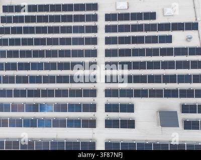 Vue aérienne rapprochée d'un grand réseau de panneaux solaires disposés en lignes diagonales sur un toit plat commercial, infrastructure d'énergie renouvelable et installation photovoltaïque Banque D'Images