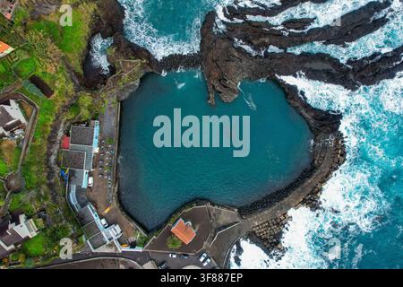 Vue aérienne de la piscine naturelle volcanique de Seixal entourée de rochers noirs escarpés et de vagues turquoise le long de la côte de Seixal, Made Banque D'Images