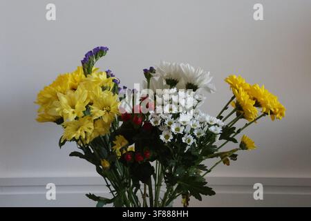 Bouquet de fleurs mélangées fraîches mettant en avant des fleurs jaunes et blanches, des accents violets et des baies rouges disposés sur un fond neutre simple avec généro Banque D'Images