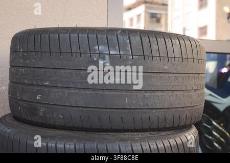Plan rapproché au niveau des yeux détaillant le motif de la bande de roulement, les canaux d'eau profonds et la texture du caoutchouc des pneus automobiles empilés à l'extérieur près d'une éolienne d'atelier Banque D'Images