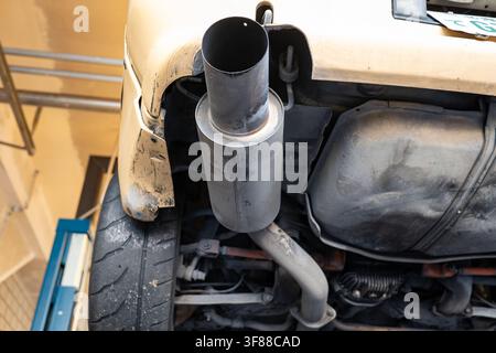 Plan rapproché en faible angle détaillant le silencieux d'échappement unique en forme de canon, le réservoir d'essence, la liaison de suspension arrière et le large pneu arrière sur une voiture surélevée sur un hyd Banque D'Images