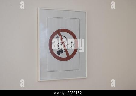 Un panneau «interdiction de fumer» encadré présentant un cercle de prohibition rouge classique au-dessus d'une cigarette allumée, fixé sur un mur blanc simple dans un environnement intérieur. Banque D'Images