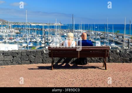 Couple mûr assis sur un banc profitant de la vue sur une marina par une journée ensoleillée, îles Canaries, Espagne, Europe Banque D'Images