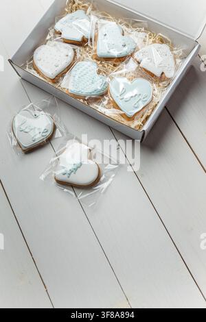 Biscuits gingersnaps de Noël dans une boîte. Formes de cœurs et de pulls. Sucreries hivernales glacées sur fond en bois blanc. Espace pour du texte Banque D'Images