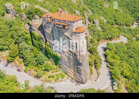 Vue aérienne par drone du monastère de Rousanou perché sur une falaise verticale avec une route asphaltée sinueuse en contrebas par une journée ensoleillée dans la région de Météora à Kalambaka T Banque D'Images