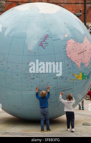 Deux enfants explorent « Le monde à l'envers », un globe inversé de Mark Wallinger à la London School of Economics (LSE). Banque D'Images