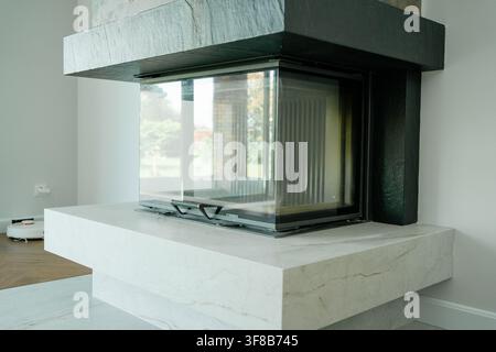 Cheminée d'angle minimaliste construite en pierre avec une hotte sombre dans un intérieur de maison lumineux. Photo d'archive parfaite pour la chaleur de la maison, intérieur Banque D'Images