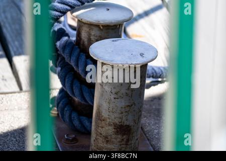 Corde tressée bleue enroulée autour d'un bittement en métal dans une marina, illustrant le travail maritime et les responsabilités du quai. Banque D'Images