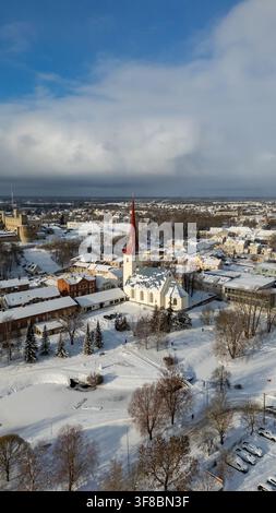 Vue aérienne de l'église de la Trinité de Rakvere avec son clocher rouge, entourée de toits enneigés et du château historique de Rakvere à Rakvere, L Banque D'Images