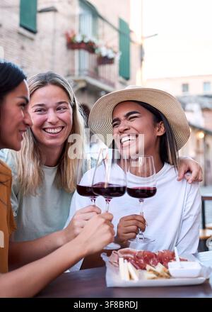 Trois amies féminines heureuses grillent avec du vin rouge en plein air dans la ville italienne Banque D'Images