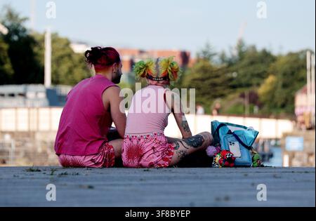 Fluidité de genre et expression de soi, deux individus non binaires aux cheveux colorés et aux tatouages assis en plein air. Diversité et inclusion en milieu urbain Banque D'Images