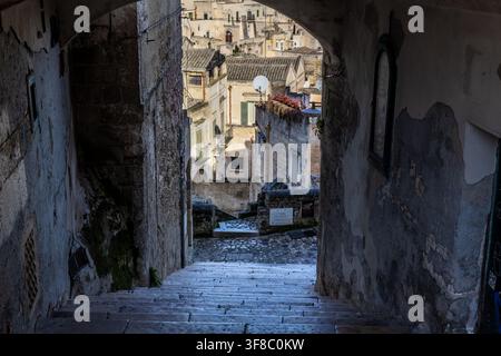 Vue d'un escalier étroit en pierre menant à travers une ruelle ancienne vers les Sassi di Matera historiques, avec des murs en pierre usés et traditionnels Banque D'Images
