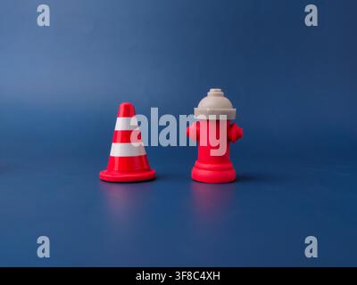 Un petit cône de signalisation avec des rayures rouges et blanches est posé à côté d'une bouche d'incendie jouet rouge sur du papier bleu. Banque D'Images