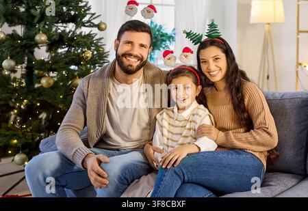 Portrait de famille joyeux avec fille sur le canapé portant des bandeaux de Noël amusants Banque D'Images