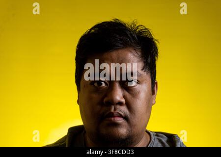 Portrait rapproché d'un jeune homme asiatique regardant directement la caméra avec une expression faciale sérieuse et neutre. L'homme a des cheveux courts et foncés et un Banque D'Images