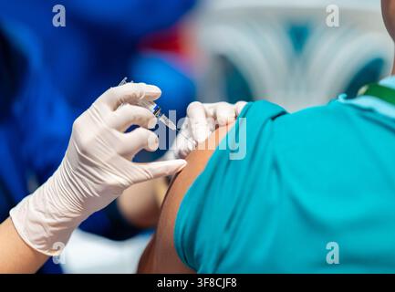Grossissement d'un professionnel de santé portant des gants blancs de protection administrant une injection de vaccin dans le bras supérieur d'un patient dans un environnement clinique Banque D'Images