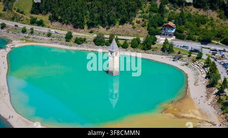 Vue aérienne du clocher submergé de Curon émergeant des eaux turquoise du lac de Reschen, entouré de montagnes verdoyantes à Reschen am See, Tr Banque D'Images