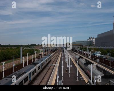 Train de voyageurs et train de marchandises passant par la gare de Cambridge South avec le MRC Laboratory of Molecular Biology (LMB) au loin Banque D'Images