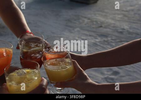Close-up de mains portant des toasts à des boissons lors d'une fête sur la plage au coucher du soleil, concept de célébration de vacances. Banque D'Images